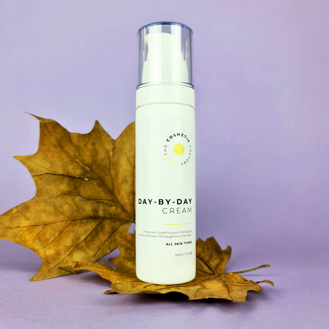 a bottle of day-by-day cream 50ml on a purple surface on top of a leaf.