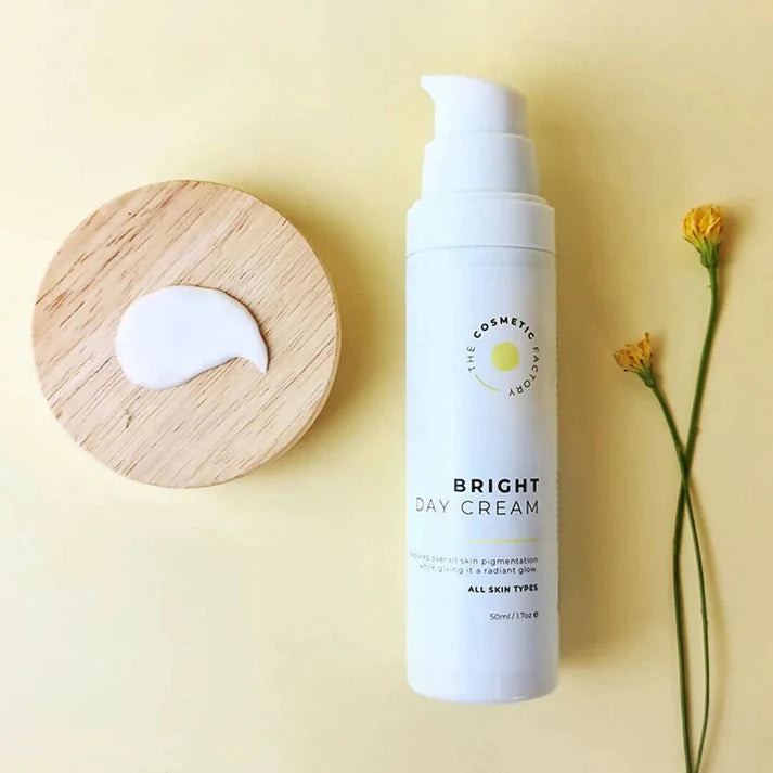 a bottle of bright day cream 50ml on a yellow surface next to flowers.