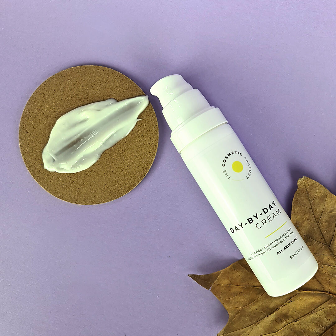 a bottle of day-by-day cream 50ml on a purple surface on top of a leaf.